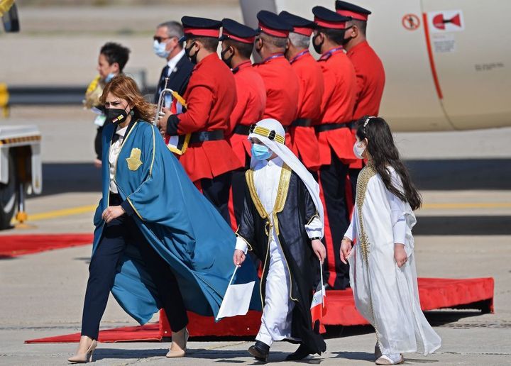 Iraqi children dressed in traditional outfits join a protocol member wearing a protective mask as they welcome Pope Francis a