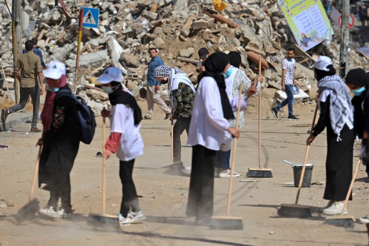 Palestinian volunteers sweep the rubble of buildings, recently destroyed by Israeli strikes, in Gaza City's Rimal district on