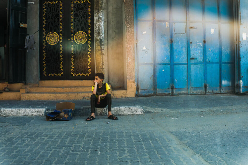 A child seen sitting on a sidewalk on Gaza’s longest and fastest road, Salah El-Deen Street, near Jabalia. Gaza, August, 2nd, 2021 (Photo: Mahmoud Nasser)