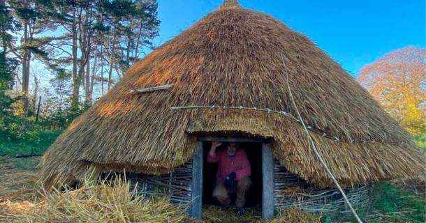 A second reconstructed roundhouse has been built by University of Dublin Centre for Experimental Archaeology students, after the first was subject to arson. Dr. Aidan O’Sullivan, crouched in the entryway of the roundhouse his students built. Source: UCD Centre for Experimental Archaeology