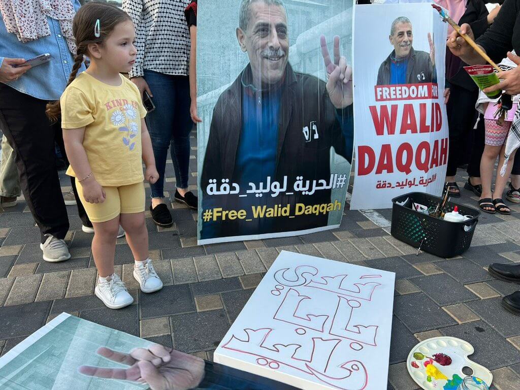 Milad Daqqa, left, standing next to a poster depicting her father, Walid Daqqa, holding up the victory sign with the sentence "Free Walid Daqqah" at the bottom, at a rally calling for his freedom.