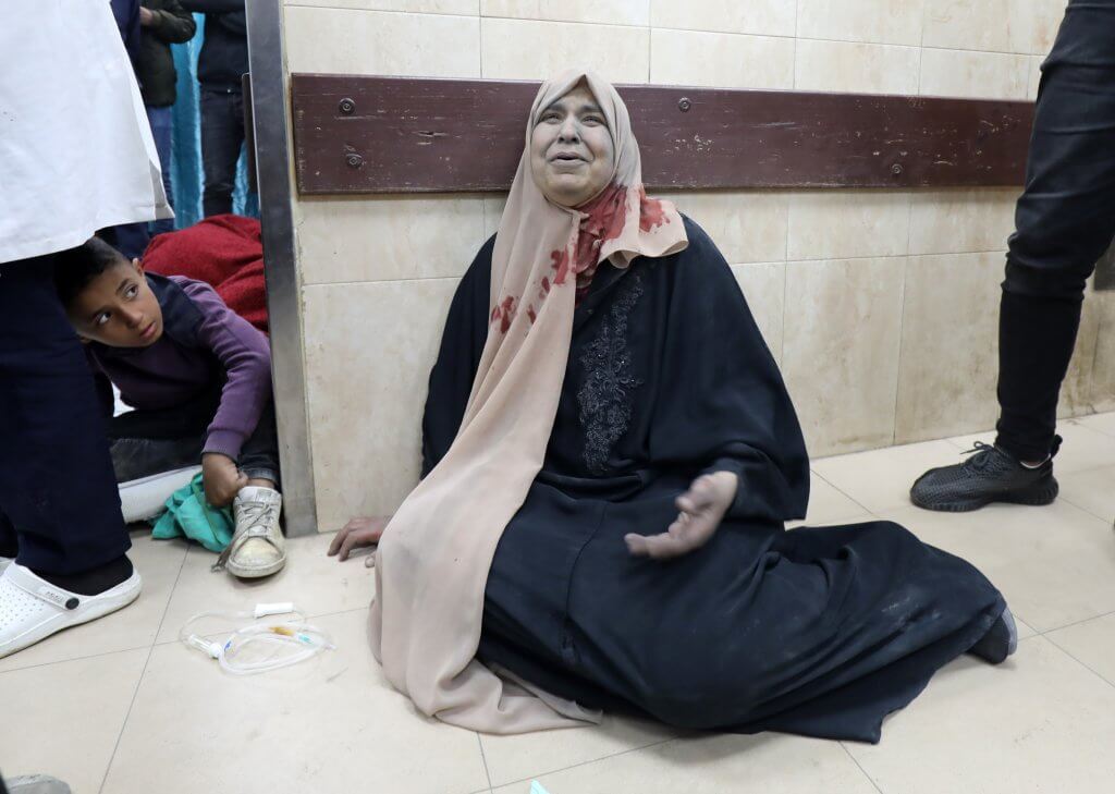 An injured Palestinian woman sits on the floor of a hospital in Gaza covered in blood and dust